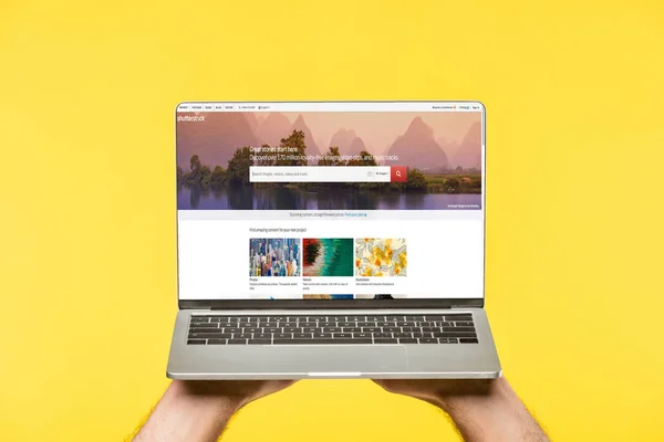 裁剪拍摄的人拿着笔记本电脑与百叶窗网站在屏幕上隔离在黄色 — 图库照片
