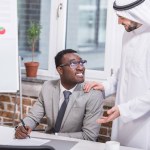 Empresario afroamericano sosteniendo pluma y mirando al socio árabe en la oficina