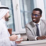 African american businessman looking at arabian partner with cup of coffee