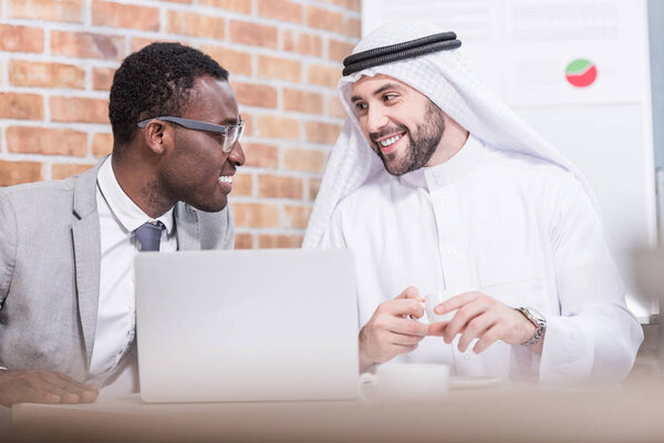 Arabian businessman looking at african american partner and smiling in office 