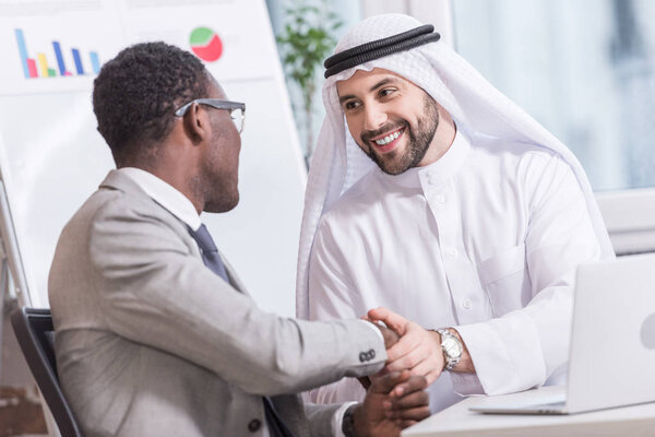 Arabian businessman shaking hands with african american partner in office 
