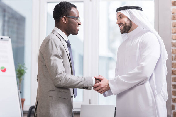 Multicultural businessmen smiling and shaking hands in modern office 