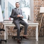 Guapo hombre de negocios sentado a la mesa y sosteniendo la taza de café en la oficina