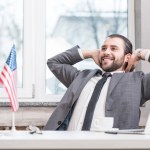 Successful businessman with hands on head sitting at office desk