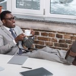 Afroamericano uomo d'affari con tazza di caffè mettendo piedi in ufficio
