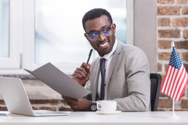 Afrika kökenli Amerikalı işadamı ofiste klasör ve kalem tutan 