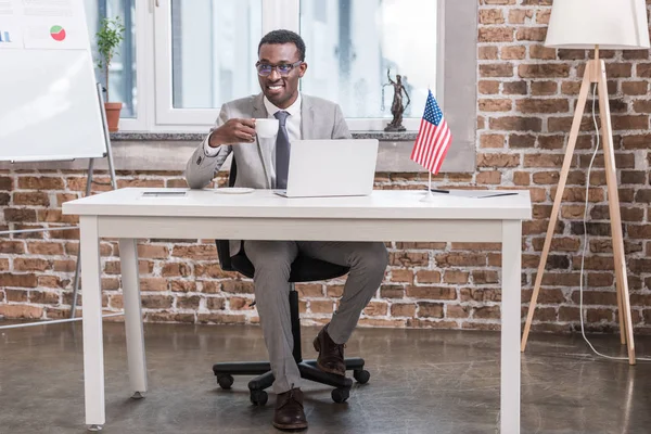 アフリカ系アメリカ人のビジネスマンのオフィスの机に座って コーヒーを飲みながら  — 無料ストックフォト