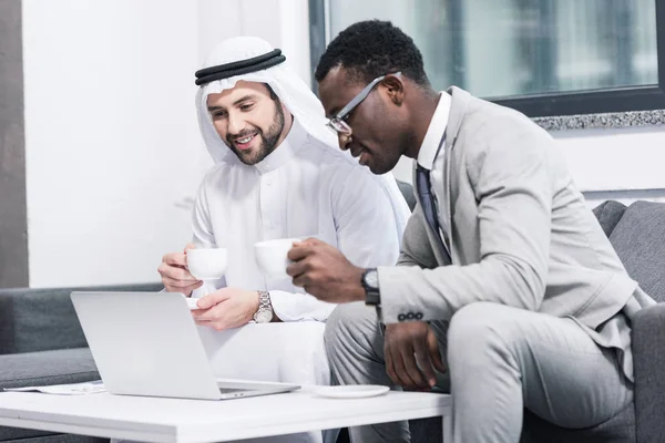 Empresarios Multiculturales Sosteniendo Copas Mirando Portátil Oficina Moderna — Foto de Stock