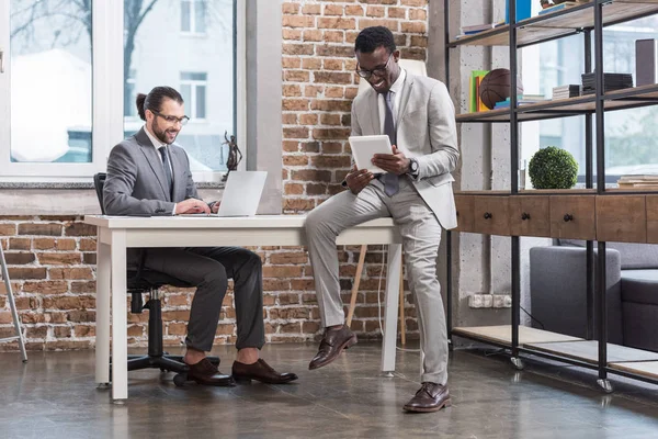 入力デジタル タブレットでテーブルの上に座ってラップトップ キーボードとアフリカ系アメリカ人ビジネスのパートナーにハンサムな男 — ストック写真