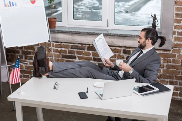 Усміхнений Бізнесмен Сидить Столом Піднімаючи Ноги Читаючи Контракт Офісі — Безкоштовне стокове фото