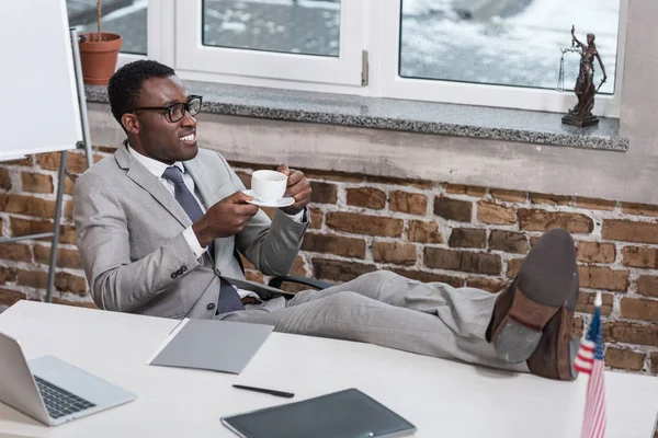 african american businessman with coffee cup putting feet up in office