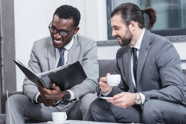 Leende Mångkulturella Affärspartners Läsa Dokument Och Dricka Kaffe Office — Gratis stockfoto