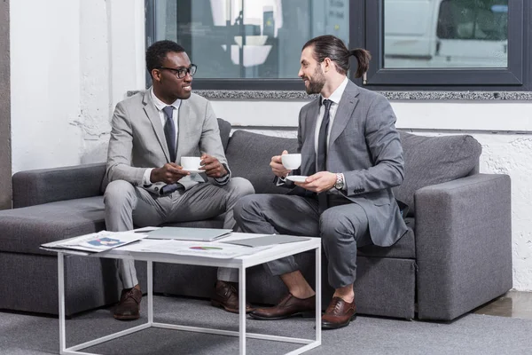 Empresarios Multiétnicos Sentados Sofá Mirándose Unos Otros Tomando Café Oficina — Foto de Stock