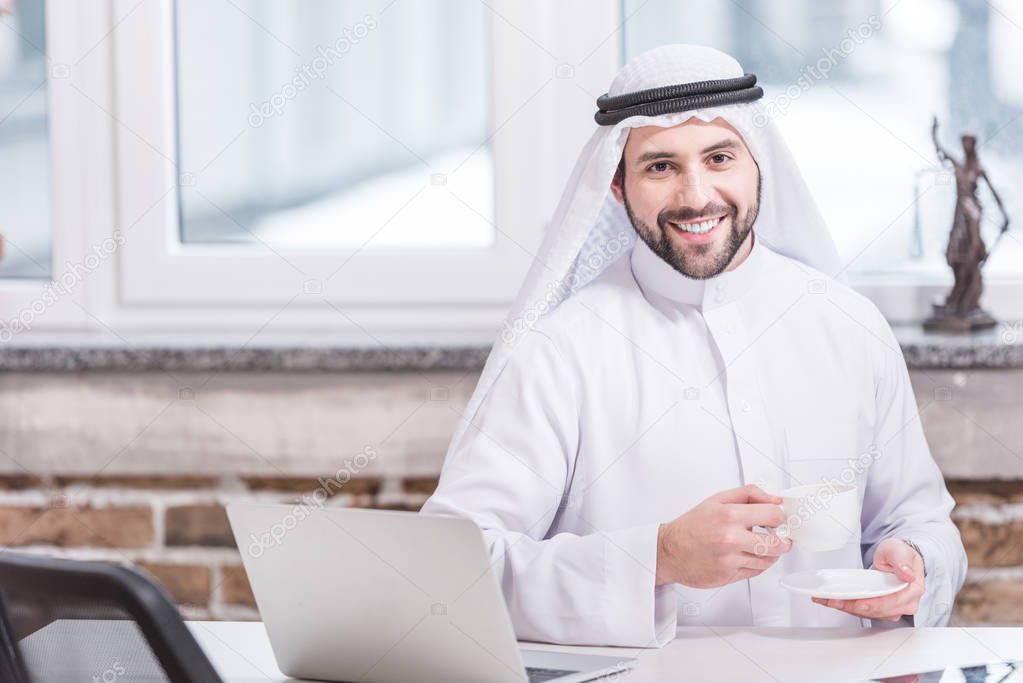 Arabian businessman drinking coffee near laptop in office 