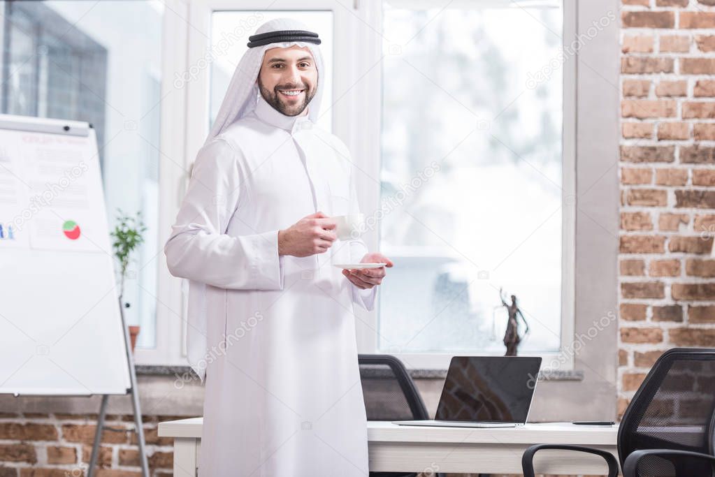 Arabic businessman holding cup with drink in modern office 