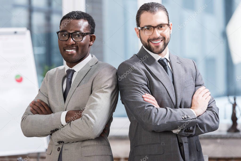 close up view of two multiethnic businessmen with arms crossed in office