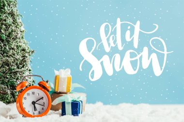 Noel hediye ile mavi arka plan ile kar üzerinde çalar saat ve minyatür Noel ağacı duran yakın çekim shot 
