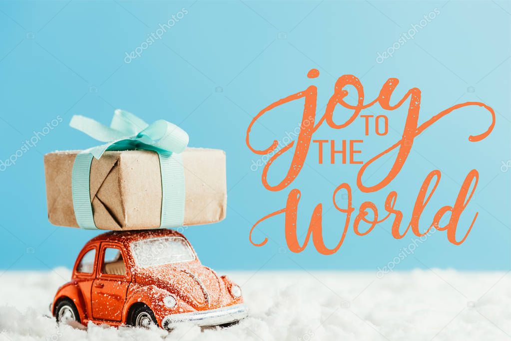 close-up shot of toy red car with christmas present riding by snow made of cotton on blue background with 