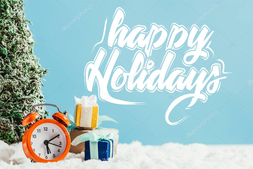 close-up shot of christmas gifts with alarm clock and miniature christmas tree standing on snow on blue background with 