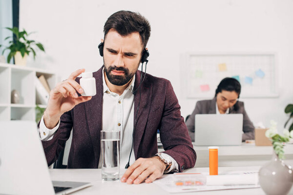 sick call center operator sitting at desk and holding pill bottle in office