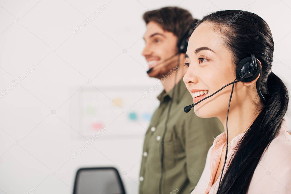 pretty call center operator smiling with handsome coworker on background in office