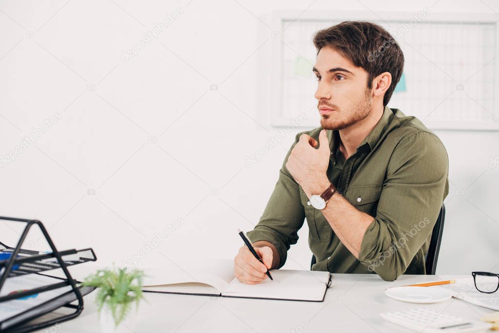 Businessman sitting at desk and thinking with pen in hand