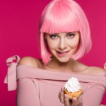 Atractivo sensual chica mordiendo el labio y sosteniendo cupcake aislado en rosa