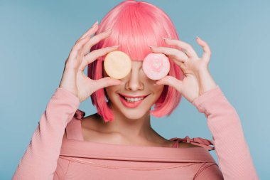 pembe peruk iki macarons mavi izole ile poz çekici gülümseyen kız