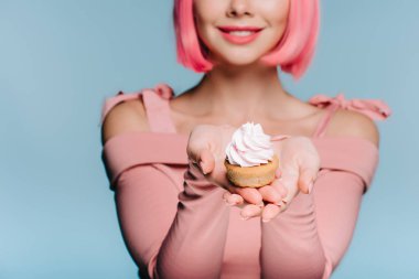 gülümseyen kız mavi izole tatlı cupcake tutarak görünümünü kırpılmış