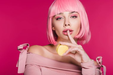 macaron tutarak ve pink izole sessizlik sembolünü gösterirken pembe peruk çekici şehvetli kız