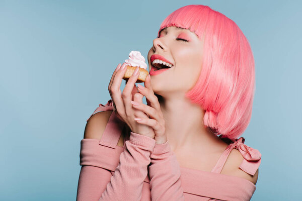 excited girl in pink wig holding sweet cupcake isolated on blue