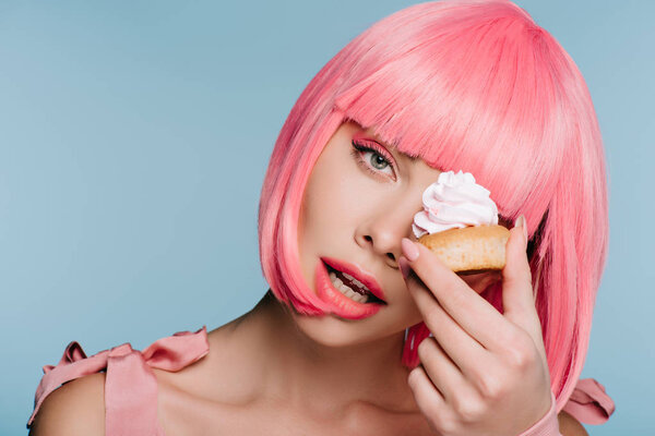 sensual young woman in pink wig posing with tasty cupcake isolated on blue
