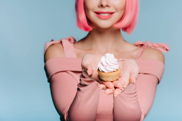 cropped view of smiling girl holding sweet cupcake isolated on blue