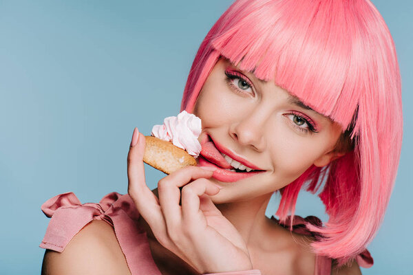 beautiful happy girl in pink wig licking sweet cupcake isolated on blue