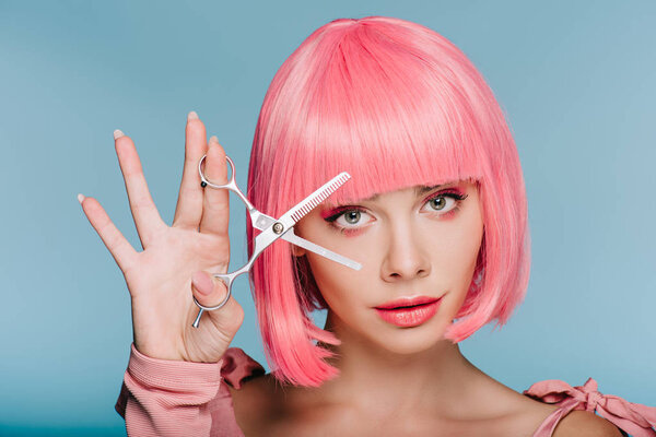 attractive fashionable girl in pink wig posing with scissors isolated on blue