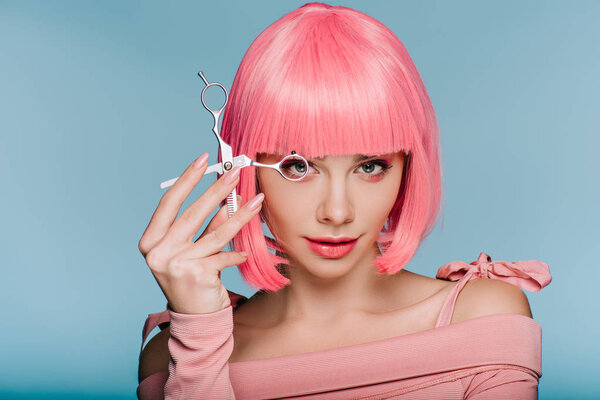 beautiful girl in pink wig posing with scissors isolated on blue