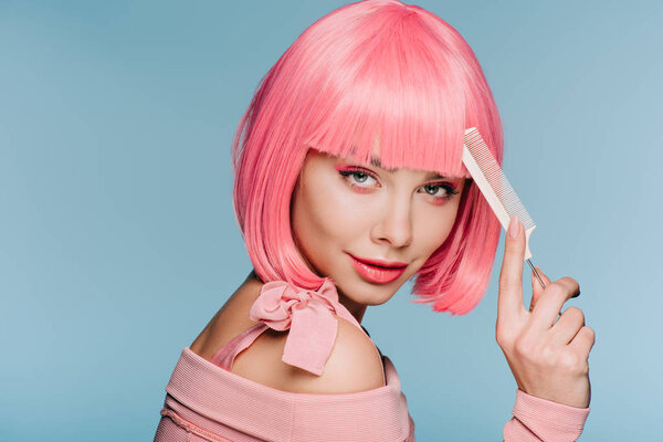 attractive girl in pink wig posing with hair comb isolated on blue