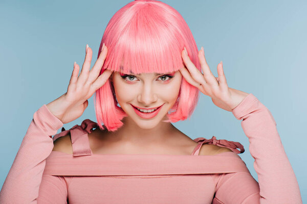 cheerful fashionable girl gesturing and posing in pink wig isolated on blue