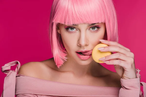有吸引力的女孩在粉红色的假发舔黄色的马卡龙孤立在粉红色 — 图库照片