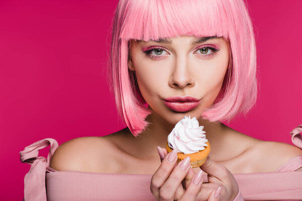 attractive girl in pink wig holding delicious cupcake with buttercream isolated on pink