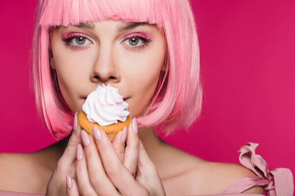 красивая девушка в розовом парике держа кекс с маслом крем изолирован на розовый
