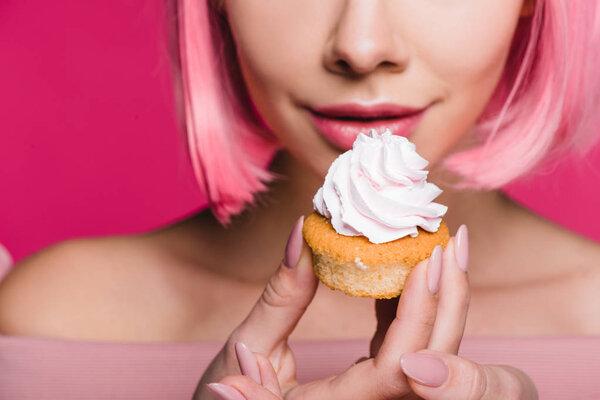 обрезанный вид чувственной девушки, держащей сладкий кекс изолирован на розовый
