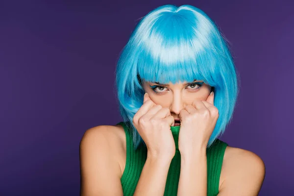 attractive girl in blue wig hiding face in green turtleneck, isolated on purple