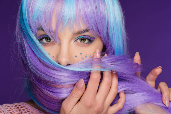 beautiful stylish girl posing in violet wig with stars on face, isolated on purple