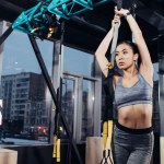 Slim asian girl in sportswear training with resistance bands at modern gym