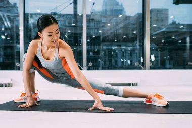gülümseyen ve spor salonunda fitness mat bacak Germe esnek Asyalı kız