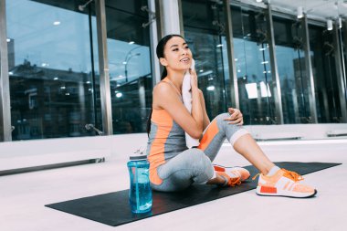 Fitness mindere oturmuş ve havlu ile yüz modern spor salonu silerek gülümseyen Asyalı kız