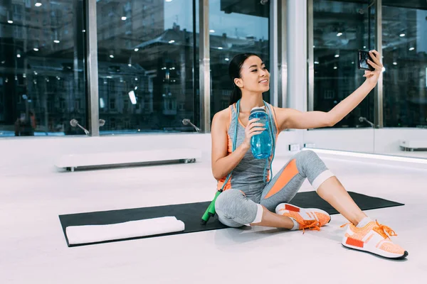 Lachende Aziatische Meisje Zit Fitness Mat Sportfles Met Water Houden — Stockfoto