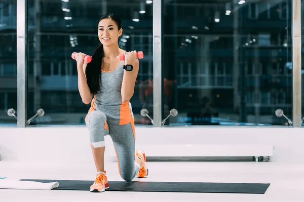 Lächelnde Asiatische Sportlerin Beim Training Mit Kurzhanteln Auf Fitnessmatte Fitnessstudio — kostenloses Stockfoto