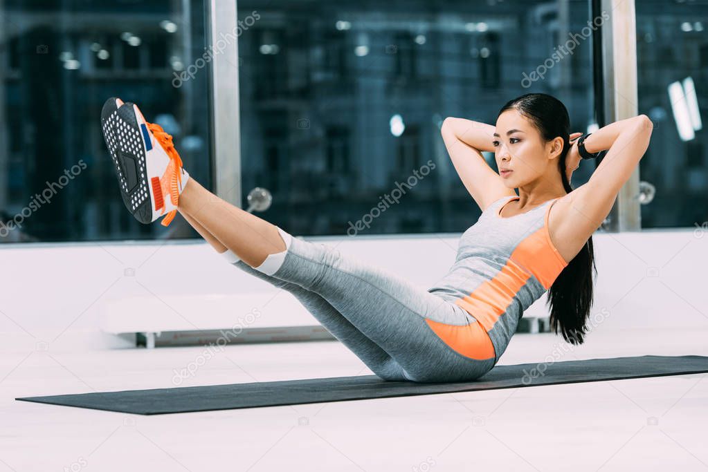 slim asian girl with hands on head training on fitness mat in sports center